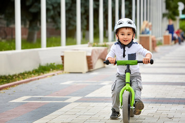Child boy in white helmet riding on his first bike with a helmet. Bike without pedals.