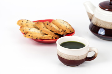 Hot green tea and home made a small sweet cookie with .black sesame, typically round, flat, and crisp.Cookie on .white.
