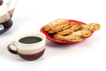 Hot green tea and home made a small sweet cookie with .black sesame, typically round, flat, and crisp.Cookie on .white.
