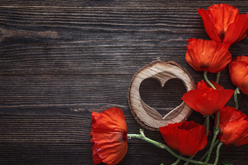 Obraz premium Czerwone maki kwiaty z drewnianym sercem na ciemnym tle drewna.