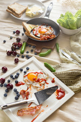 English breakfast - fried egg, bacon, bread blueberry.and cherry in frying pan on wooden board over White tablecloth background