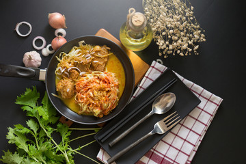 Curried Noodle Soup with spicy coconut milk and beef In a black pan On a black wood table