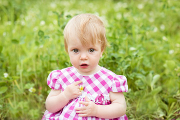 Portrait of a beautiful baby girl sitting on green meadow