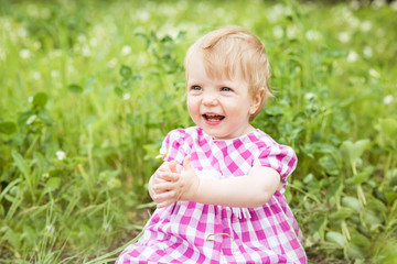 Portrait of a beautiful baby girl sitting on green meadow