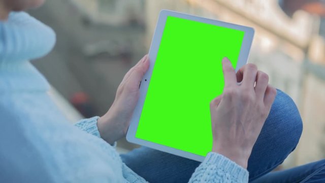 Young Woman in blue sweater sitting near window uses Tablet PC with pre-keyed green screen. Few types of gestures - scrolling up and down, tapping, zoom in and out. Perfect for screen compositing