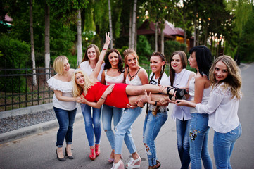 Fototapeta premium Crazy company of bridesmaids holding bride in red dress in the park at bachelorette party.