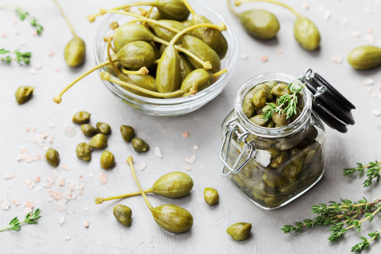 Mixed capers in jar and bowl on gray kitchen table from above.
