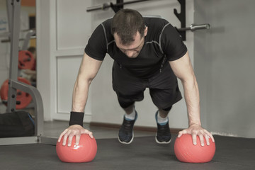 Fototapeta na wymiar Fitness man doing push-ups exercise on the ball in gym