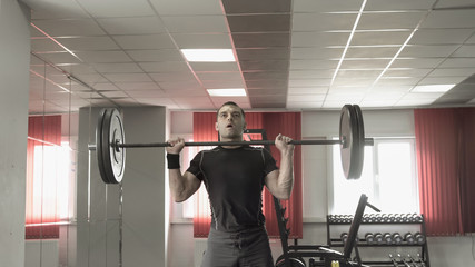 Young man doing exercise with a barbell in gym.