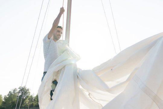 Man on sailing boat, taking down sail