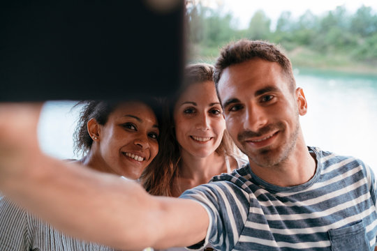 Three friends outdoors, taking selfie with smartphone