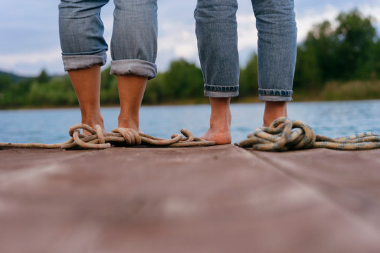 Two women, standing on pier, barefoot, low section, rear view