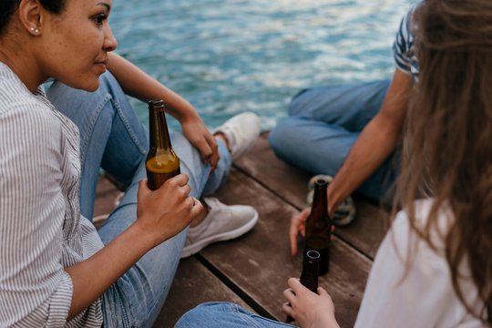 Three friends relaxing on pier, holding bottles of beer