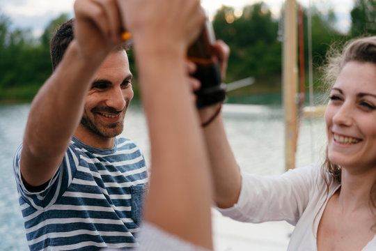 Three friends beside lake, holding bottles of beer, making a toast