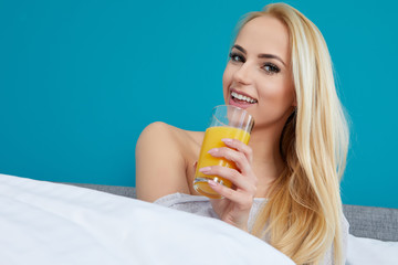 Attractive woman drinking orange juice sitting on her bed