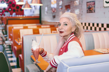 Portrait of mature woman in baseball jacket with milkshake in 1950's diner
