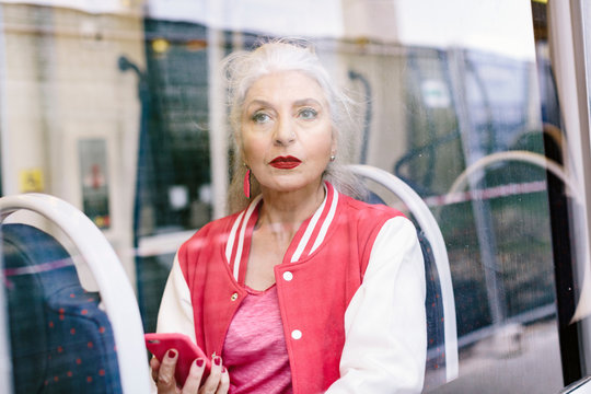 Mature woman in baseball jacket looking through window from bus
