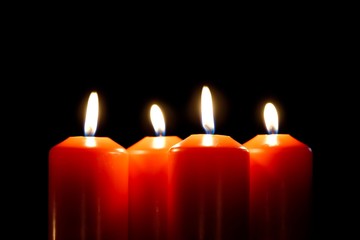 Closeup of four burning candles isolated on black. One candle in focus