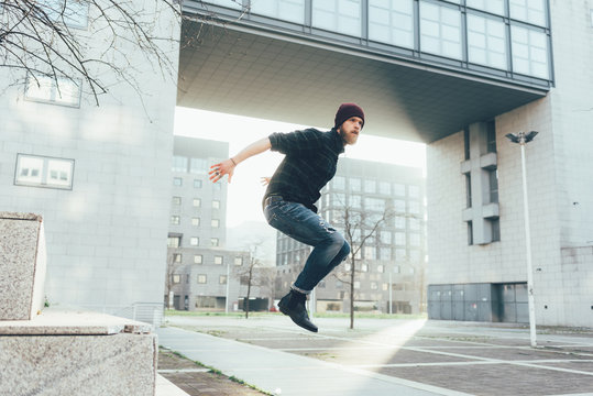 Young male hipster jumping mid air practicing parkour in city