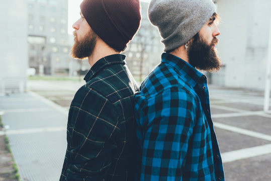Portrait of two young male hipsters in knit hats back to back in city