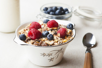 Closeup of cereal breakfast with raspberries and blueberries next to orange juice.
