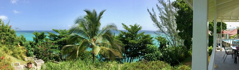 Luxurious tropical resort (hotel) with blue sky, white patio, lush green palm trees & blue ocean in...
