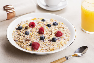 Cereal bowl breakfast with milk, raspberries and blueberries next to orange juice and cup of coffee.