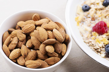 Cereal bowl breakfast with milk, raspberries and blueberries next to bowl with almonds.