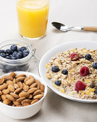 Cereal bowl breakfast with milk, raspberries and blueberries next to orange juice and bowl with almonds. Vertical studio shot.