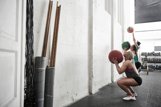 Friends throwing fitness ball against wall in cross training gym