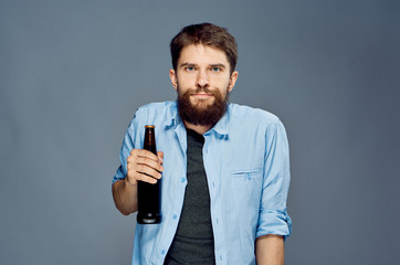 A young guy with a beard on a gray background holds a bottle of beer, alcohol