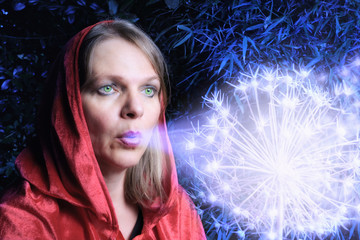 Frau mit roter Kapuze pustet auf leuchtende Blume