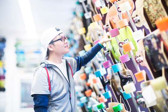 Young male skateboarder looking at rows of skateboards on shop wall