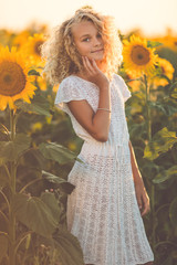 Happy pretty blonde girl in white dress having fun in field of yellow sunflowers