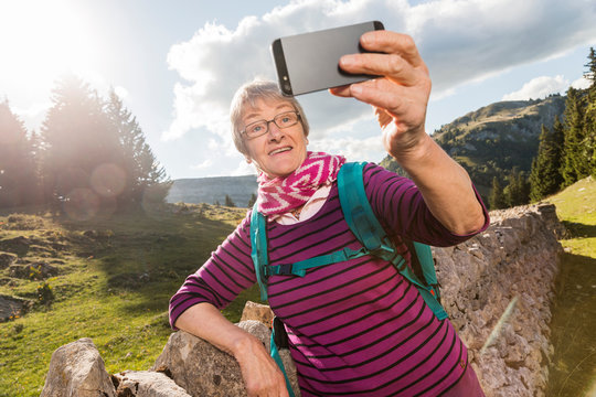 Senior woman, leaning against wall in rural setting, taking selfie, using smartphone, Geneva, Switzerland, Europe