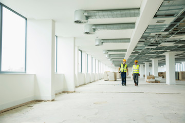 Two workers wearing hi vis vests, walking through newly constructed office space