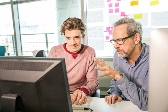 Male digital designer explaining design to trainee at office desk