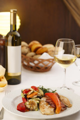 Chicken with bacon and grilled vegetables arranged on a plate, Wine bottle and wineglass in background, Traditional dish in elegant setting, Selective focus with soft light