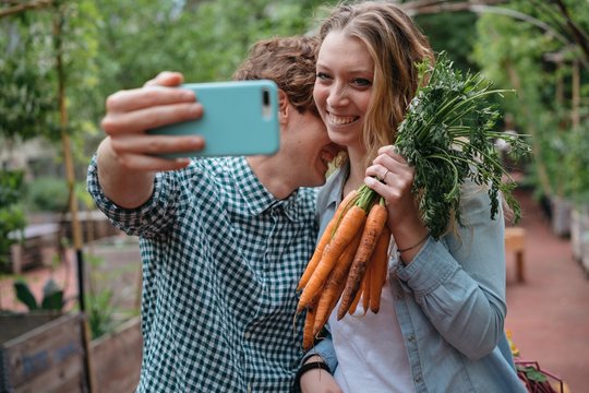 Couple in garden with carrots, taking selfie