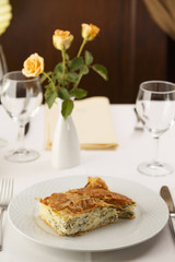 Cheese and spinach pie arranged on a plate, Wineglass in the background, Traditional dish in elegant setting, Selective focus with soft light