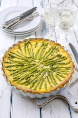 Tart with green asparagus on backing form as top view on wooden table