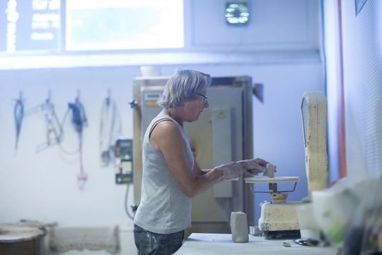 Senior woman in pottery workshop, weighing clay for pottery project