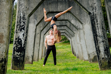 Young woman balancing on top of man hands, practicing yoga below concrete bridge