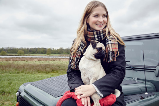 Young woman sitting on off road vehicle in field with dog on lap