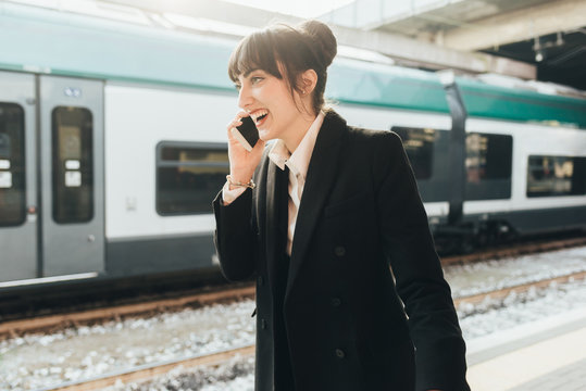 Businesswoman using mobile phone in train station, Milan, Italy