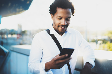 Closeup view of Happy smiling African man using smartphone outdoor.Portrait of young black cheerful man texting a sms message with friends.Blurred background.