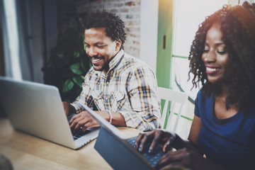African couple working at a home: black girl using touch tablet and laughing,looking through travel...