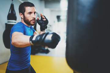 Concept of a healthy lifestyle.Young muscular man fighter practicing kicks with punching bag.Kick boxer boxing as exercise for the fight.Boxer hits punching bag.Horizontal.