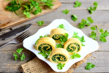 Eggs omelette rolls with cheese and greens on a plate, fork and knife on a vintage wooden table. Tasty stuffed omelette recipe. Rustic style