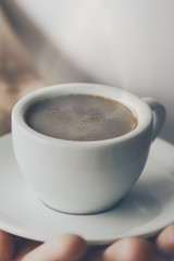 Closeup of tasty coffee espresso with tasty foam in small ceramic cup. Male hands holding warm hot drink.